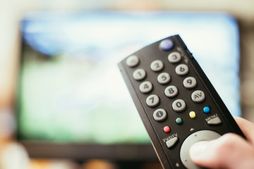 Male hand is holding TV remote control, streaming on a smart TV.