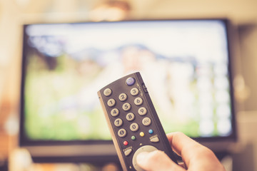 Male hand is holding TV remote control, streaming on a smart TV.