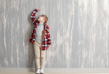 Cute little girl measuring height near grey wall