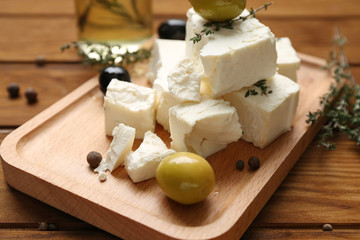 Plate with tasty feta cheese and olives on wooden table, closeup