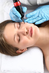 Obraz na płótnie Canvas Young woman undergoing procedure of permanent makeup in beauty salon