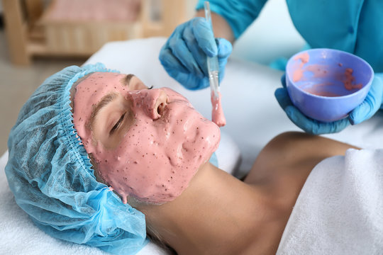 Cosmetologist applying alginate mask on young woman's face in beauty salon