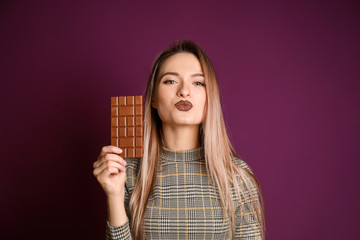 Beautiful young woman with tasty chocolate on color background