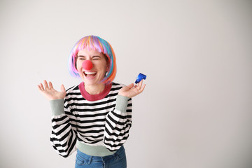 Funny woman with party whistle for April Fools' Day prank on light background