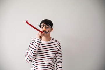 Funny Asian man with party whistle for April Fools' Day prank on light background