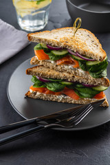 Sandwiches with cream cheese, salmon and spinach on a dark background.