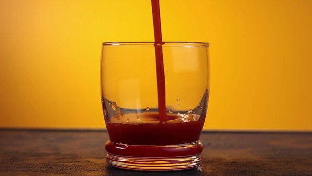 Pouring tomato bloody mary cocktail in drinking glass with water drops on dark blue concrete table with spot light. Yellow background. Slow motion video.