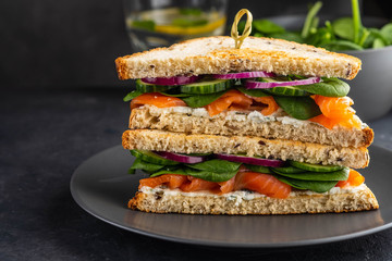 Sandwiches with cream cheese, salmon and spinach on a dark background.