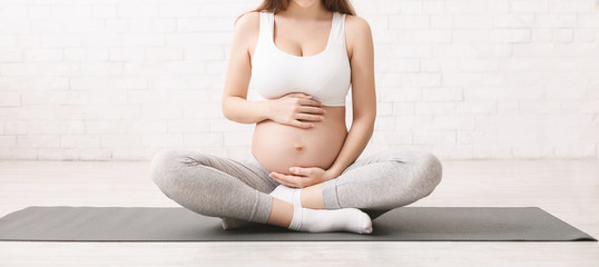 Pregnant woman meditating in lotus position at home - obrazy, fototapety, plakaty