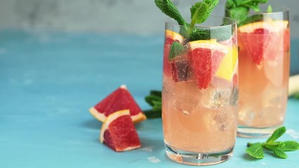 Grapefruit and fresh mint cocktail with juice, cold summer citrus refreshing drink gin tonic cocktail or beverage with ice on blue concrete surface. 59.95 fps