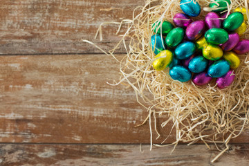 easter, confectionery and holidays concept - chocolate eggs in foil wrappers in straw nest on wooden background