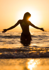 young woman walking in the sea at sunset
