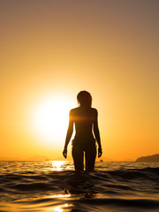 young woman walking in the sea at sunset