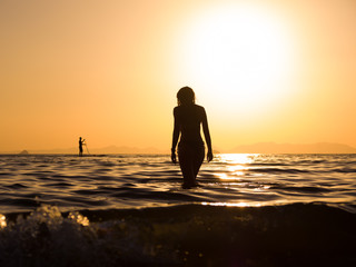 young woman walking in the sea at sunset