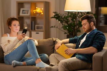 Obraz premium leisure and people concept - couple with smartphone and book at home in evening