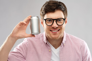 drinks and people concept - happy young man in glasses holding tin can with soda over grey...