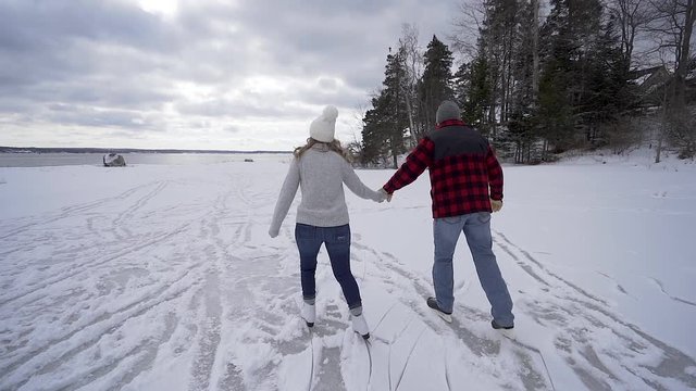 Young couple ice skates in winter on frozen pond in Maine