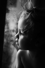 sad boy looks into the distance outside the window rain