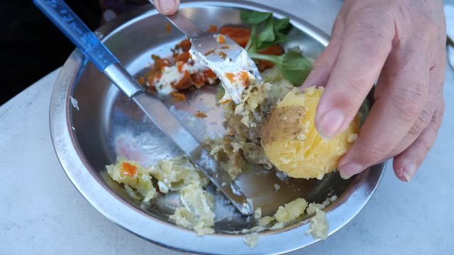 Elderly female hand peeling boiled potato with fork then mashes it and mixes it with mashed carots. Soft food for the elderly.