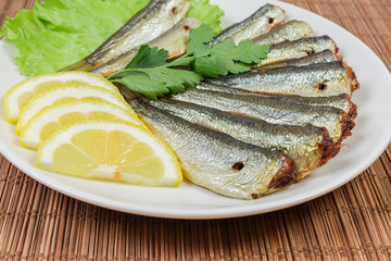 Smoked sprats, lemon, greens on a saucer close-up