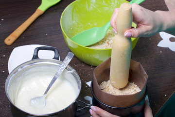 Woman adds sponge cake to cake mold. Cooking a cake of biscuit crumbs and milk jelly. On the surface of the table are the ingredients and cooking utensils.