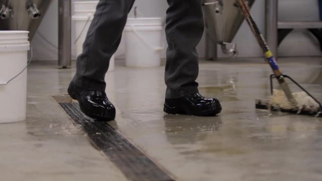 Medium shot of a worker sweeping liquid off the ground in slow motion.