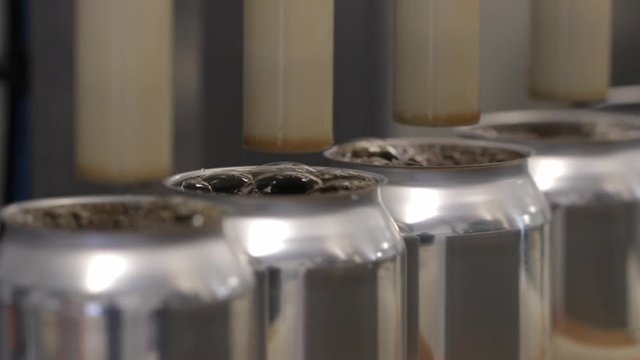 Close up of empty cans being filled by a machine on a conveyer belt as they make there way down an assembly line.