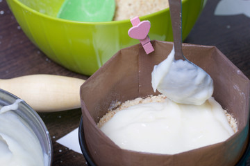 Woman adds milk jelly to cake mold. Cooking a cake of biscuit crumbs and milk jelly. On the surface of the table are the ingredients and cooking utensils.