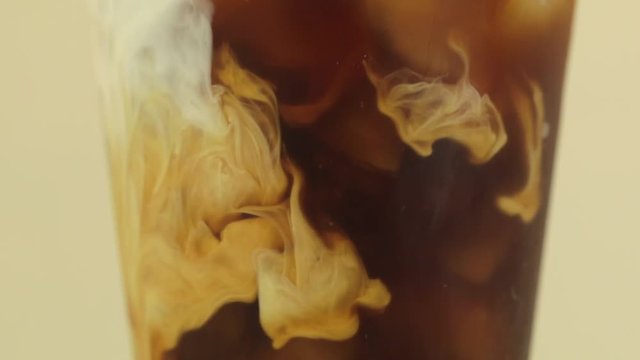 Close up shot of cream being poured into an iced coffee in slow motion.