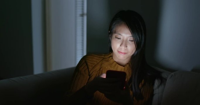 Woman use of cellphone and sit on sofa at night