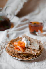 Stack of home made delicious blini of buckwheat flour served with fresh smoked salmon and sour cream. Gourmet breakfast. White knitted plaid as backgound Maslenitsa, Russia Mardi gras France