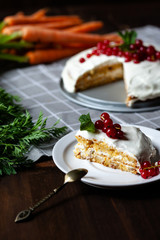 Delicious home made carrot cake with cream topping. decorated with red currant and mint. Fresh carrot with green tops. Dark brown background, grey napkin. Healthy meal