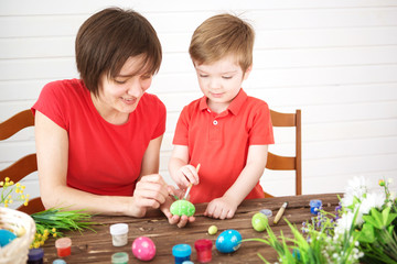 Mother and her son painting colorful Easter eggs. Happy family Mom and children son paint easter eggs with colors. Preparation for holiday.