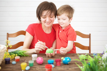 Young mother and her son having fun while painting eggs for Easter. Happy family Mom and children son paint easter eggs with colors. Preparation for holiday.