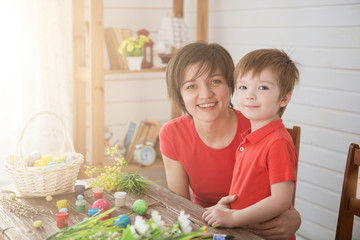 Mother and son paint eggs. Family sitting in a kitchen. Preparing for Easter. Happy family Mom and children son paint easter eggs with colors. Preparation for holiday.