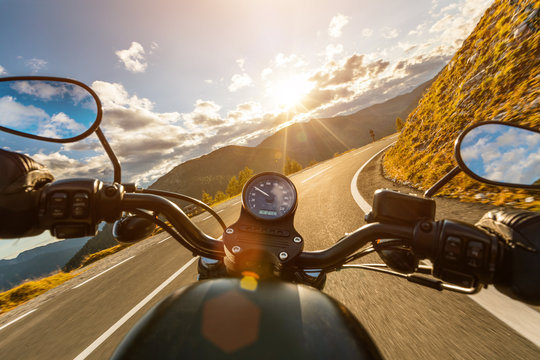 Motorcycle driver riding in Alpine highway, handlebars view, Austria, central Europe.