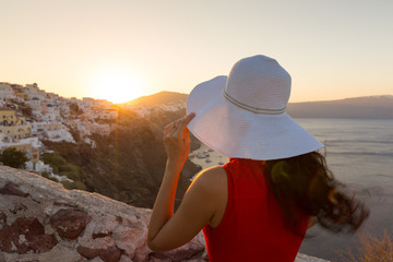 Santorini travel tourist brunette woman in red dress visiting famous white Oia village. Greece,...