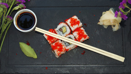 Top view of a sushi served on a black plate with sauce and sticks