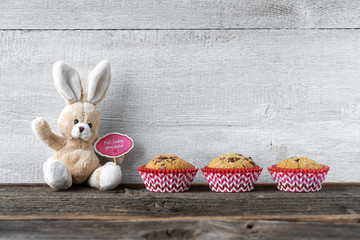 Stoffhase mit Muffins vor alter Holzwand