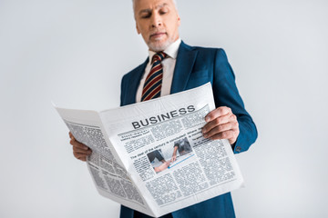 selective focus of mature businessman reading business newspaper isolated on grey