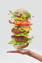 Deliciouse homemade burger on a woman hand with flying fresh ingredients on a white background....