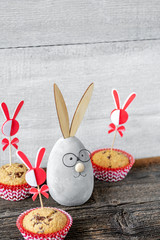 Lächelnder Dekoosterhase mit Muffinfs auf altem Holz