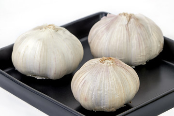Obraz premium Raw and unpeeled garlic on balck dish on white
