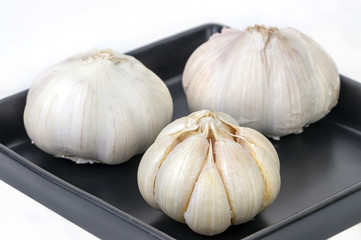 Obraz premium Raw and peeled garlic on balck dish on white