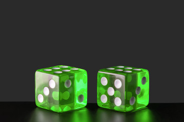 Two green glass dice on a polished wooden table on a gray uneven background with copy space. Six...