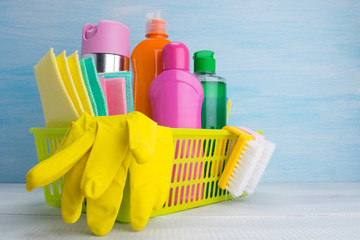 yellow basket with a set for cleaning, on a light background, gloves, bottles of cleaning products, rags, brushes
