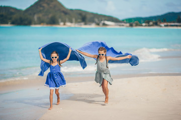 Little girls have fun with beach towel during tropical vacation