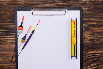 background for recording, the white sheet on the tablet lies on a wooden antique surface, with a set of items for sport fishing, floats and fishing line © kurgu128