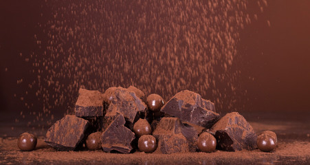 Chocolate composition. Pieces of flavored chocolate, and a round candy in the cocoa powder on dark background