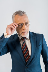 mature businessman touching glasses while standing isolated on grey